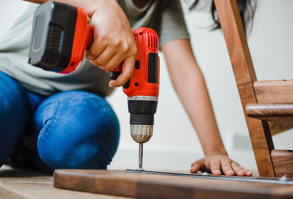 person using a drill to repair a wooden chair