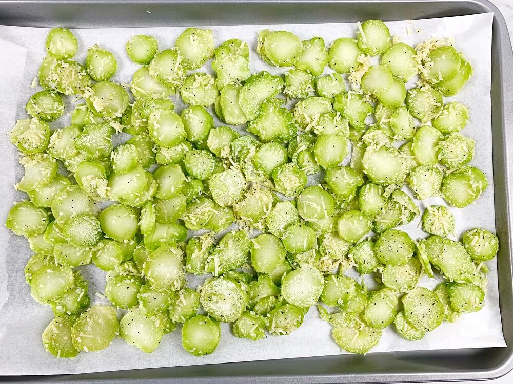Broccoli stems covered in parmesan cheese, oil, salt and pepper on a lined baking sheet