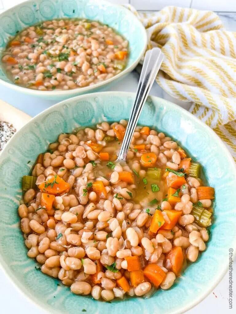 instant pot navy bean soup in a turquoise bowl with a metal spoon.